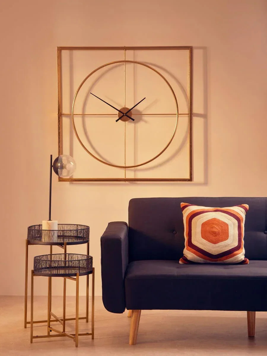 Modern wall clock with gold frame above black sofa and side tables in living room setting