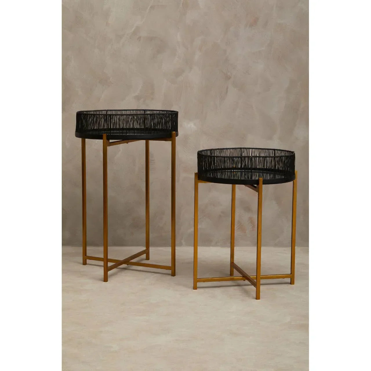 Set of two round side tables with black woven trays and gold metal legs on beige background