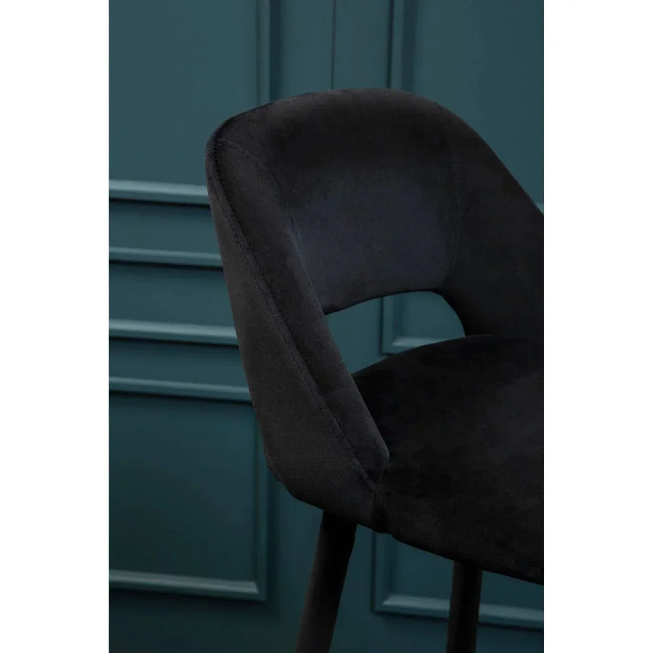 Black velvet dining chair with curved backrest against teal panelled wall