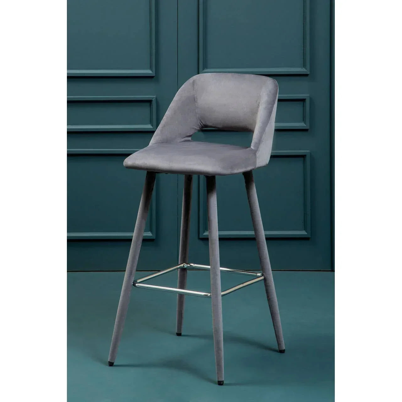 Grey velvet bar stool with metal footrest against blue panel wall