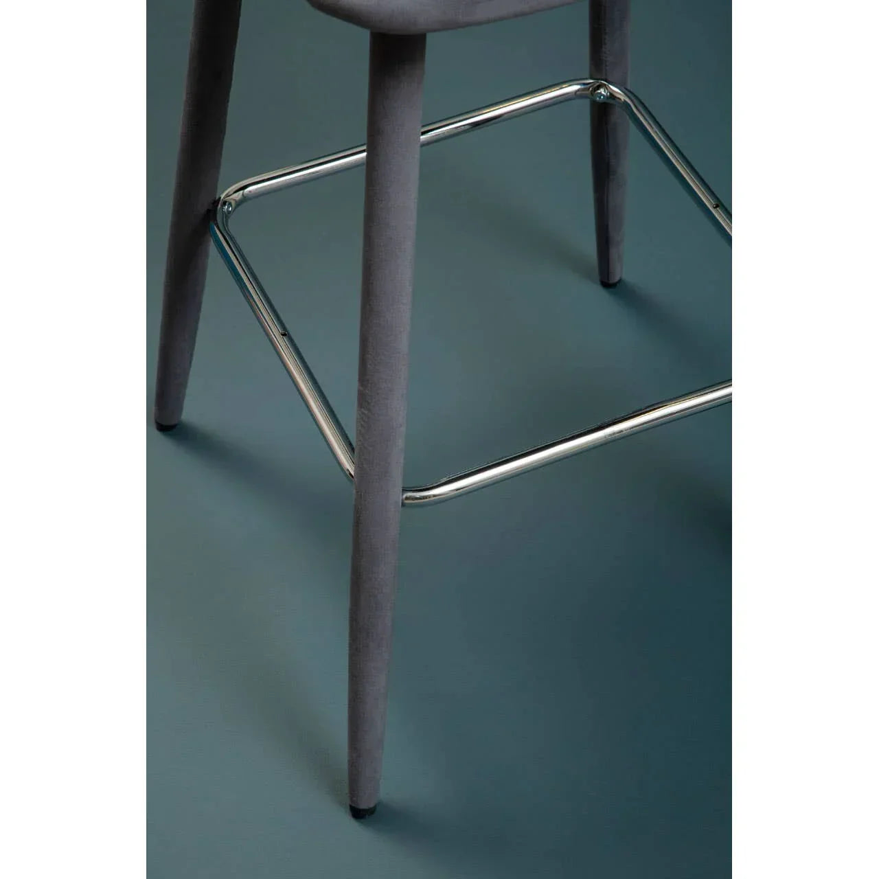 Grey bar stool legs with chrome footrest on blue floor