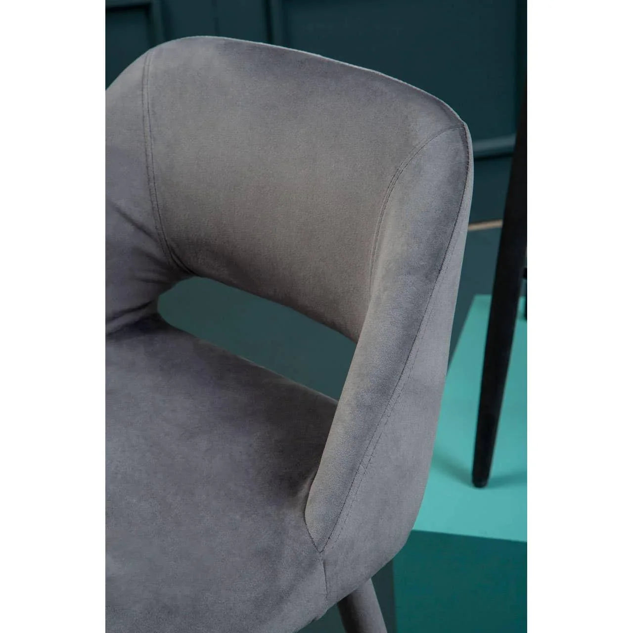Closeup of grey velvet dining chair with curved backrest against teal background