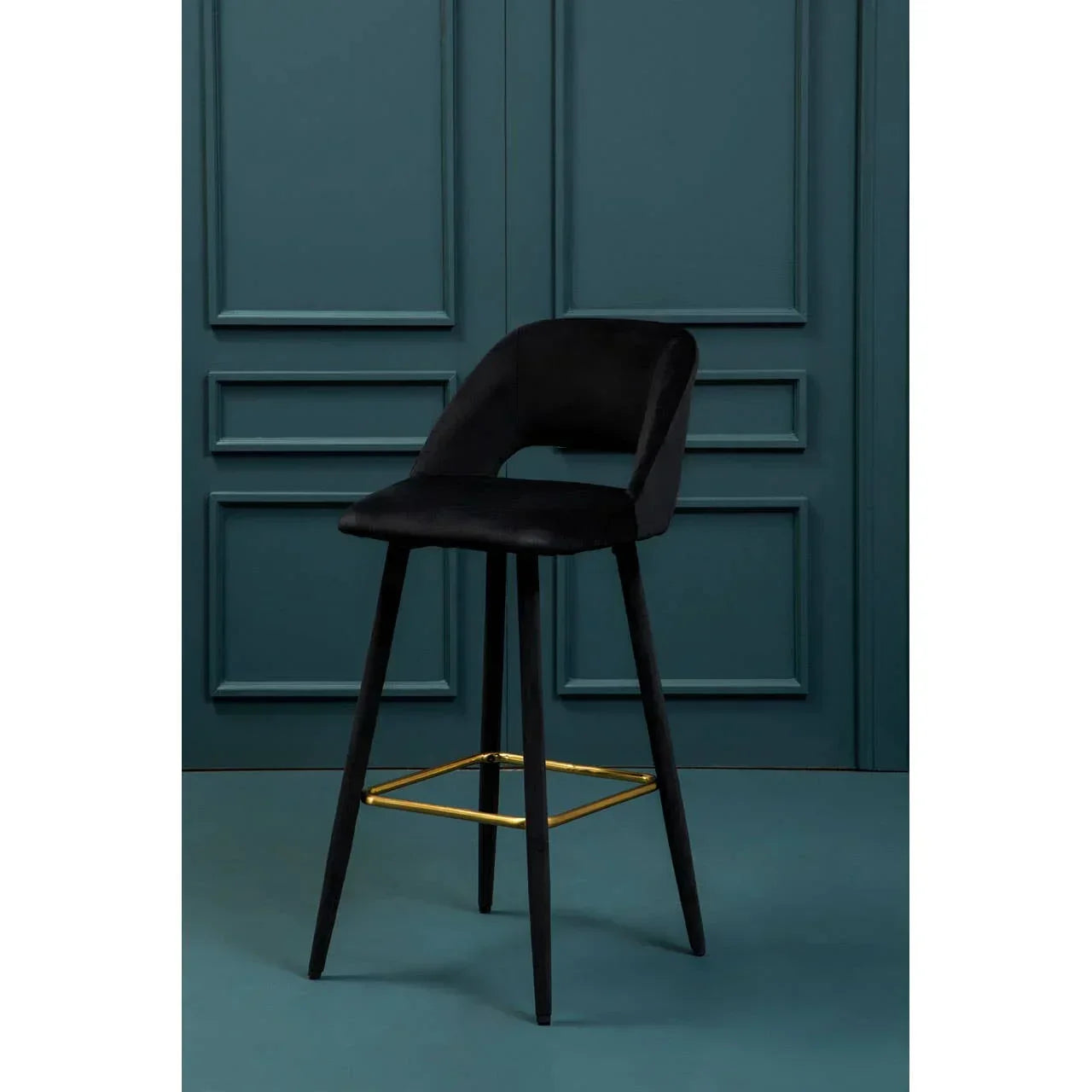Black velvet bar stool with backrest and gold footrest against teal paneled wall