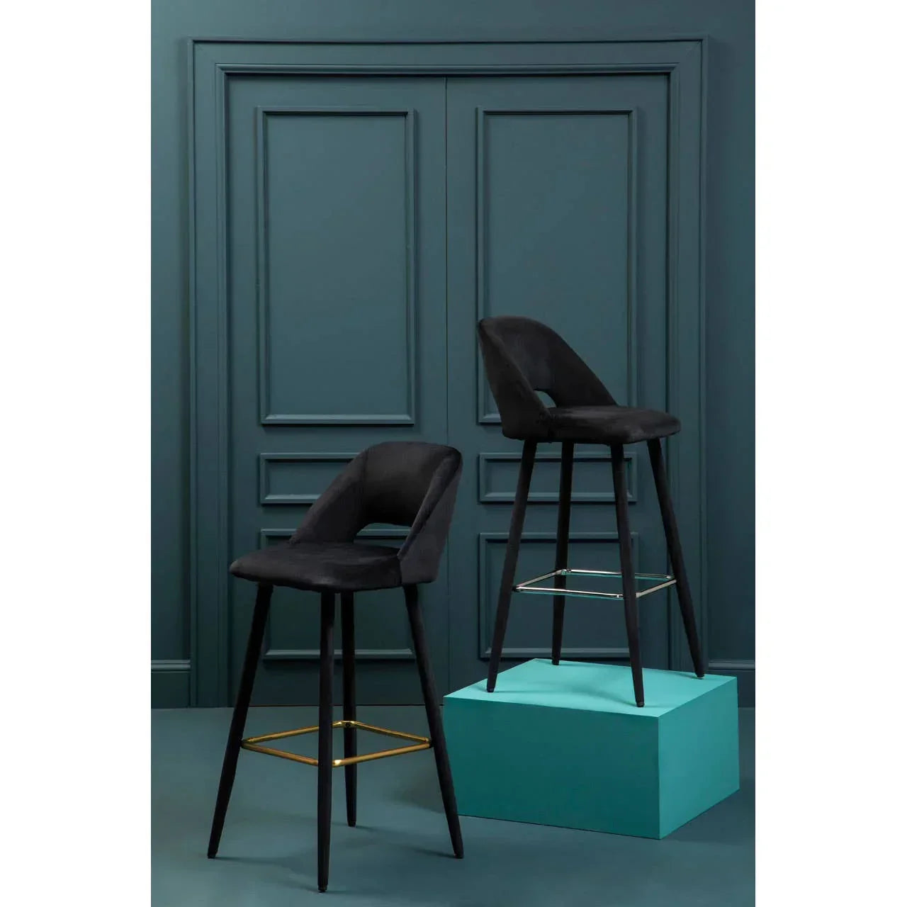 Black velvet bar stools with gold footrests against a dark teal panelled wall