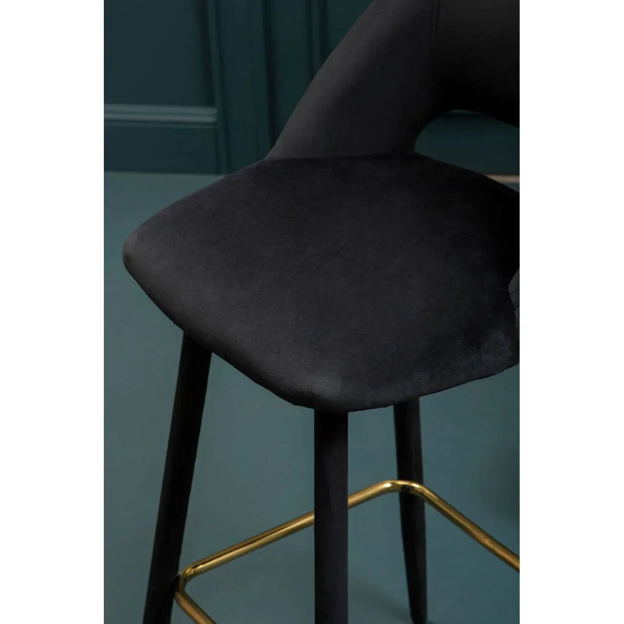 Black velvet dining chair with gold footrest and angled legs, shown in close detail