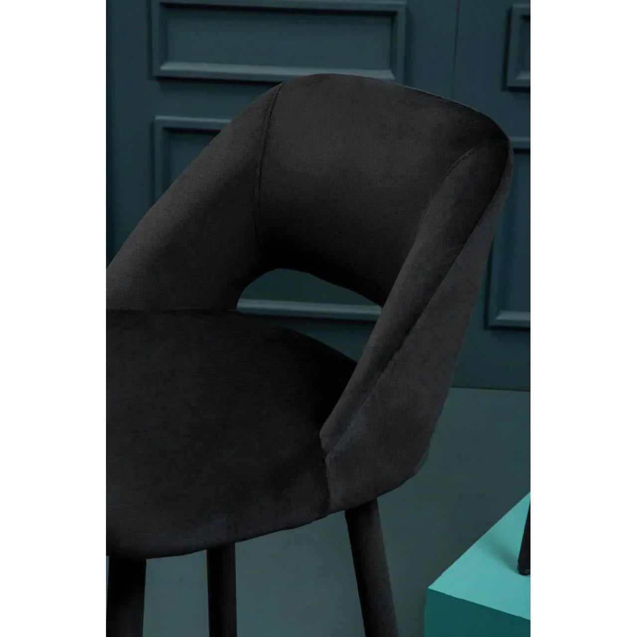 Black velvet dining chair with curved backrest against teal panel wall