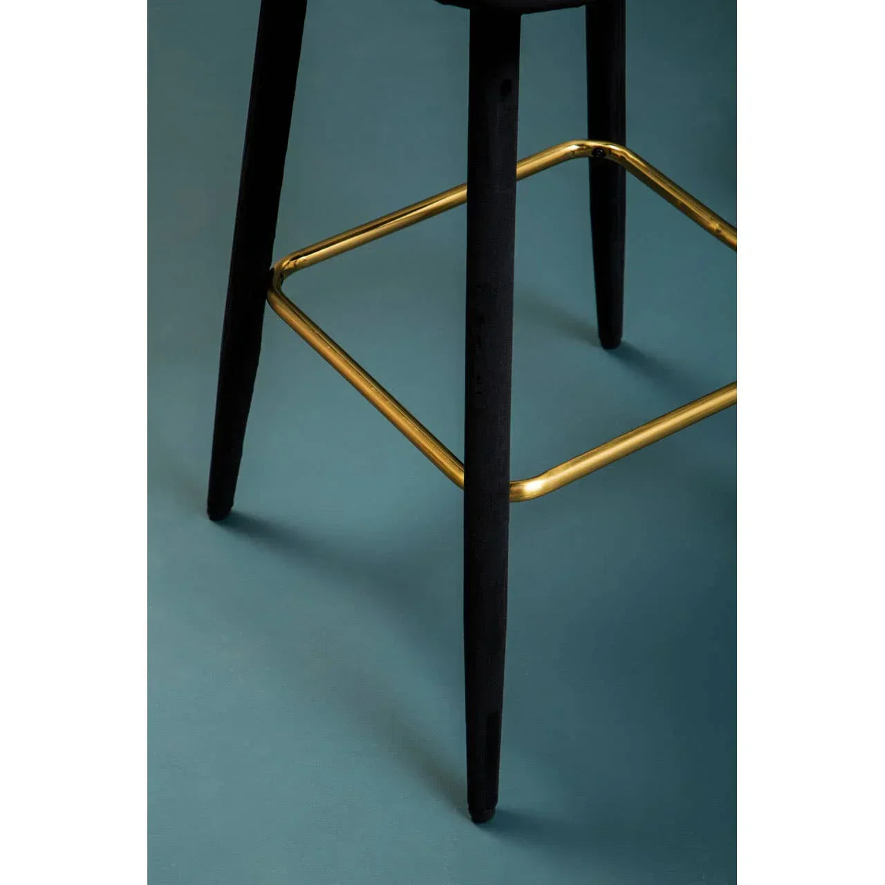 Black bar stool legs with gold metal footrest on teal floor