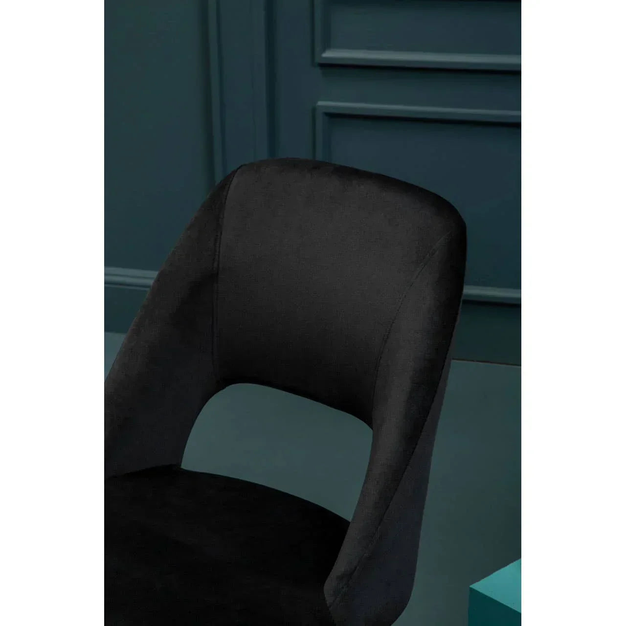 Black velvet dining chair with curved backrest against dark teal panelled wall