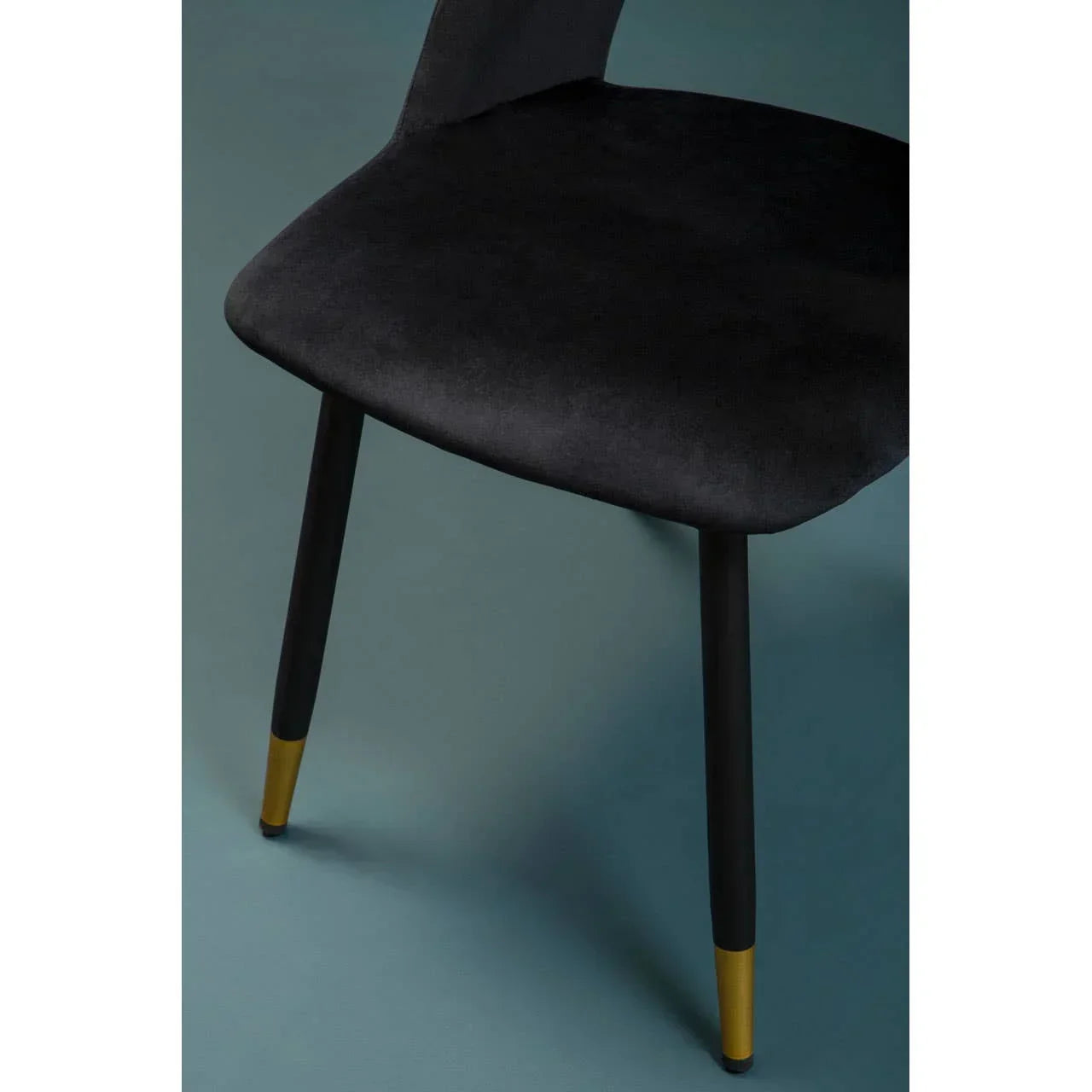 Black velvet dining chair with gold-tipped legs, side angle view on blue background