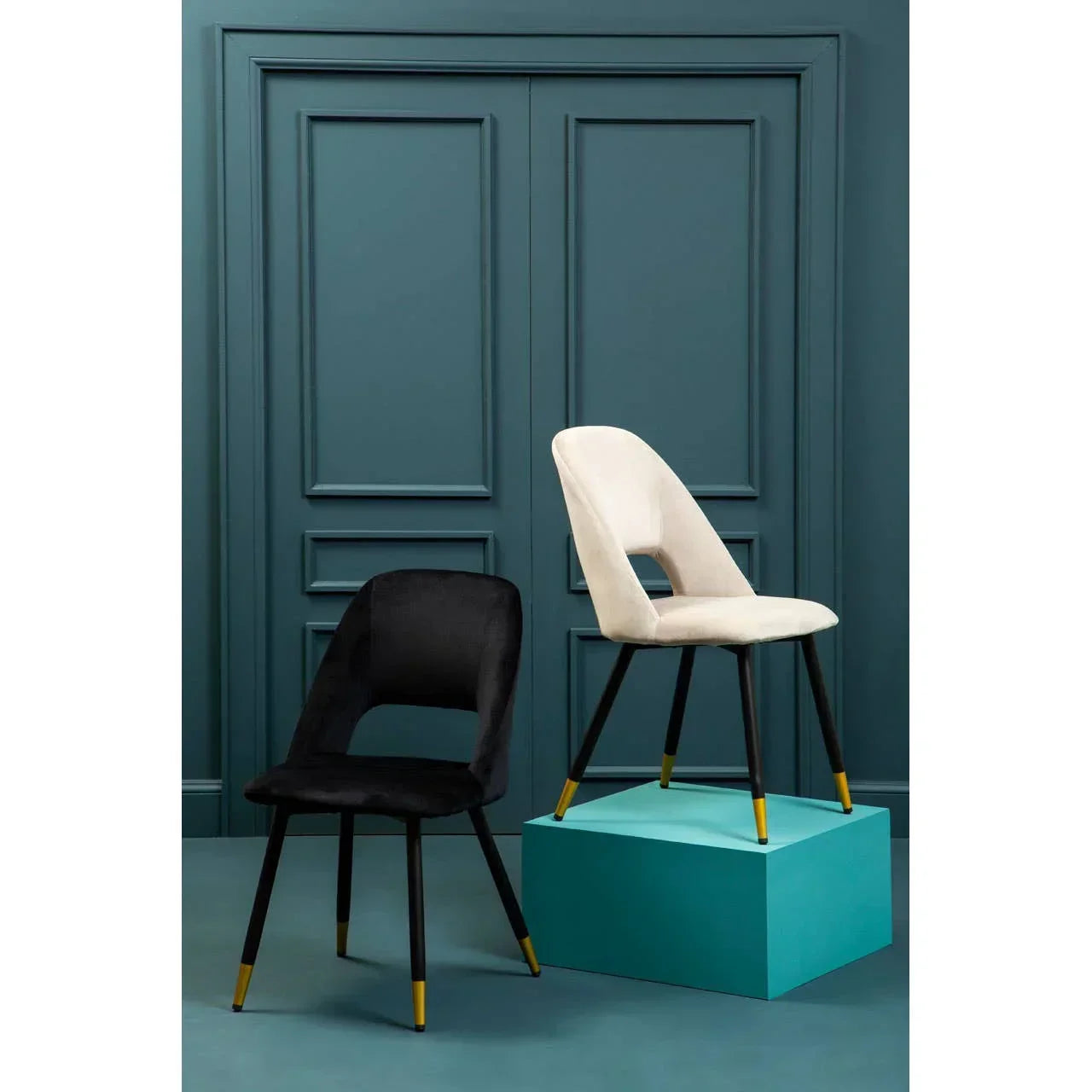 Modern dining chairs in black and cream velvet with gold leg tips against teal paneled wall