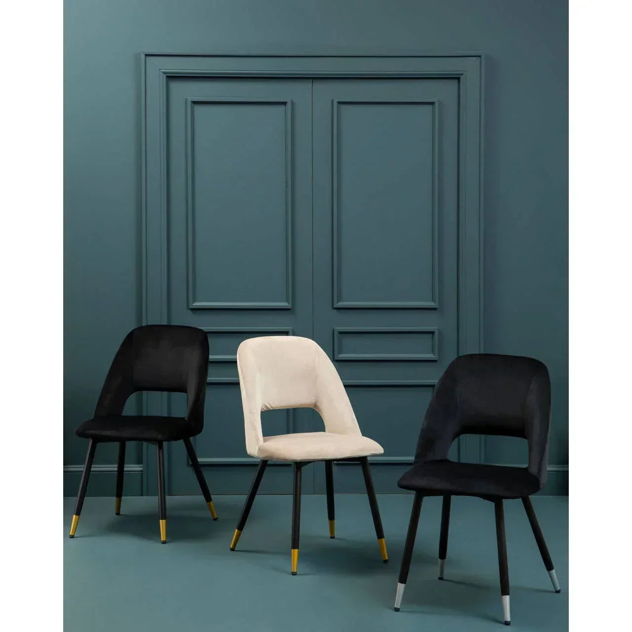 Modern velvet dining chairs with gold-tipped legs in black and cream against teal wall