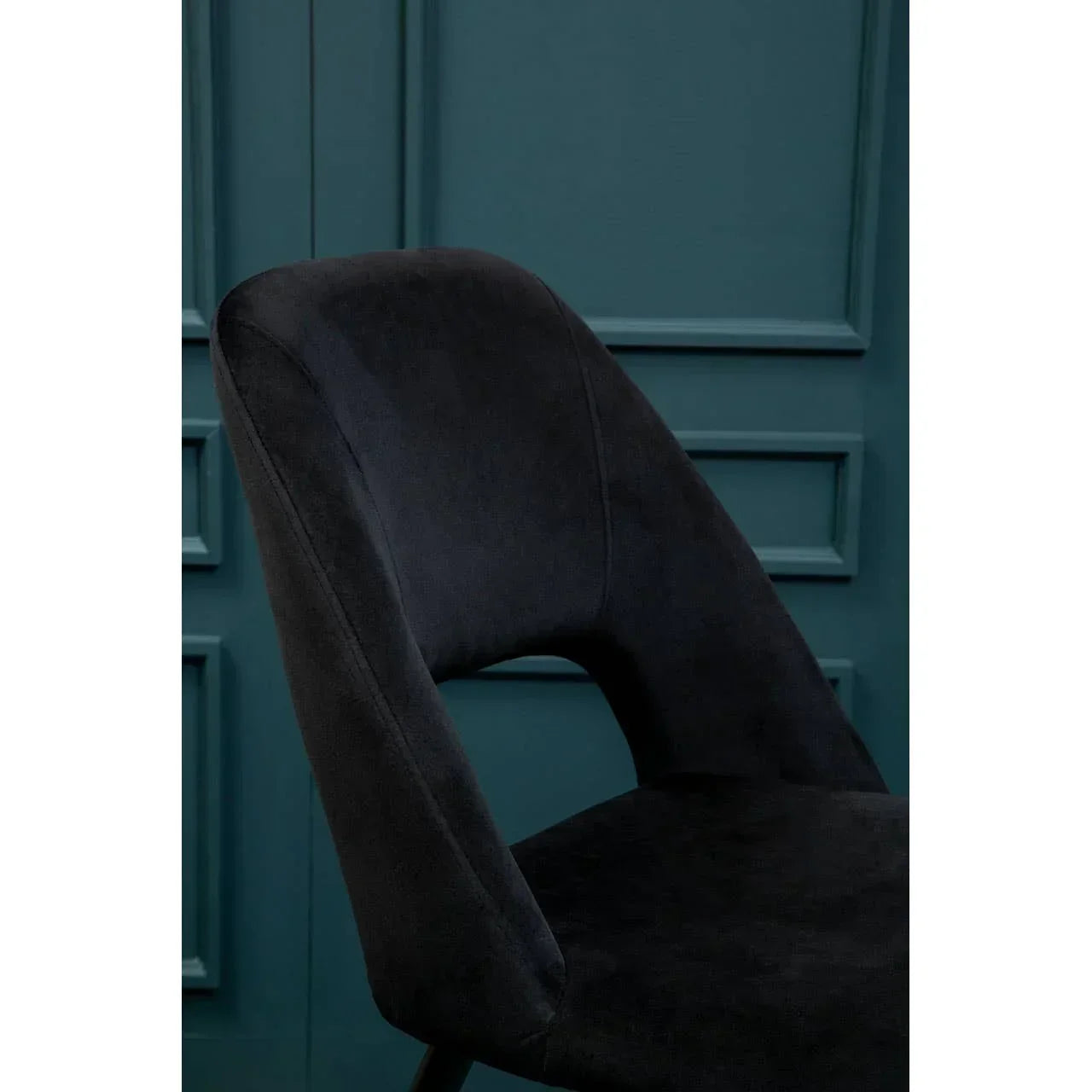 Black velvet dining chair with curved backrest against teal panel wall