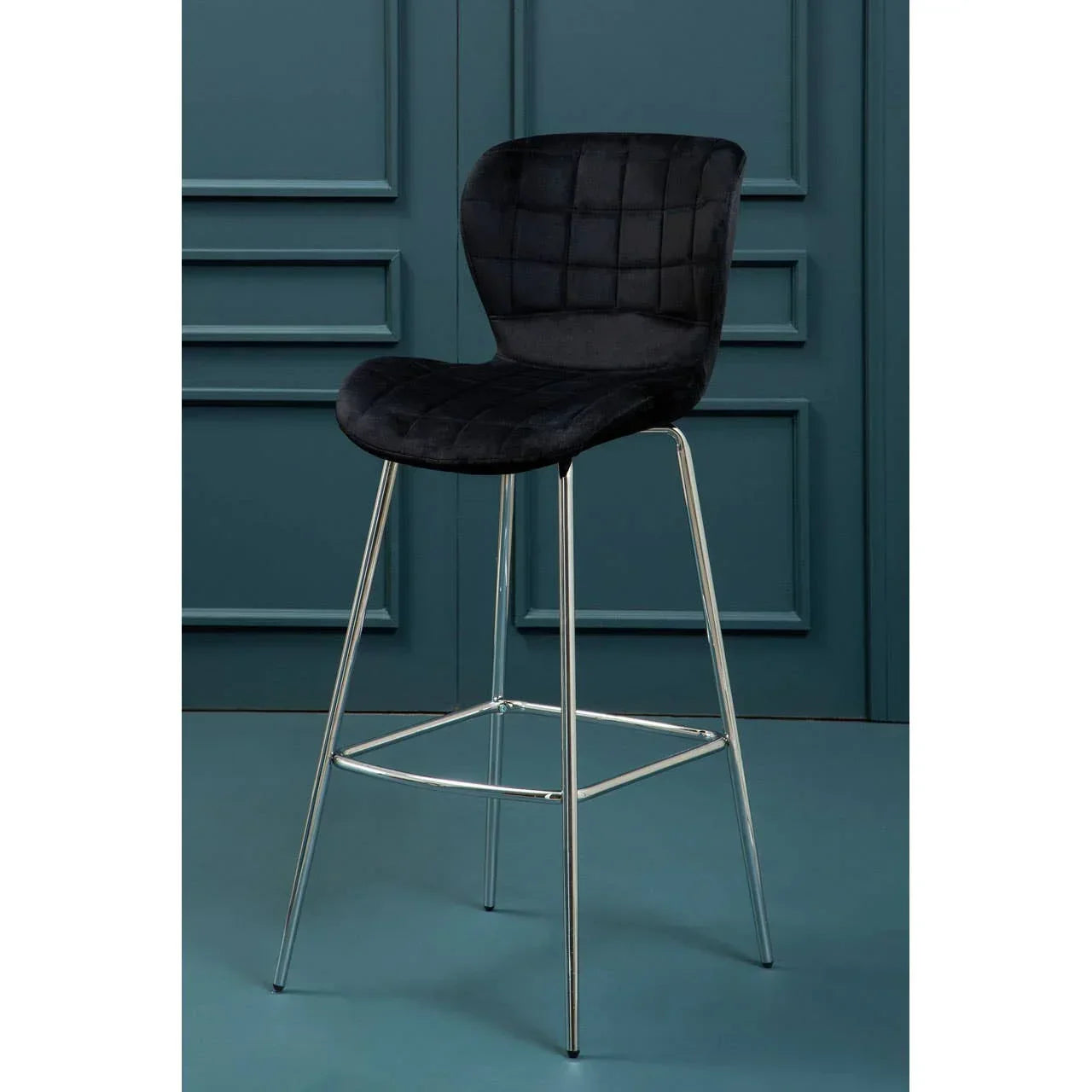 Black velvet bar stool with chrome legs and quilted backrest against blue panel wall