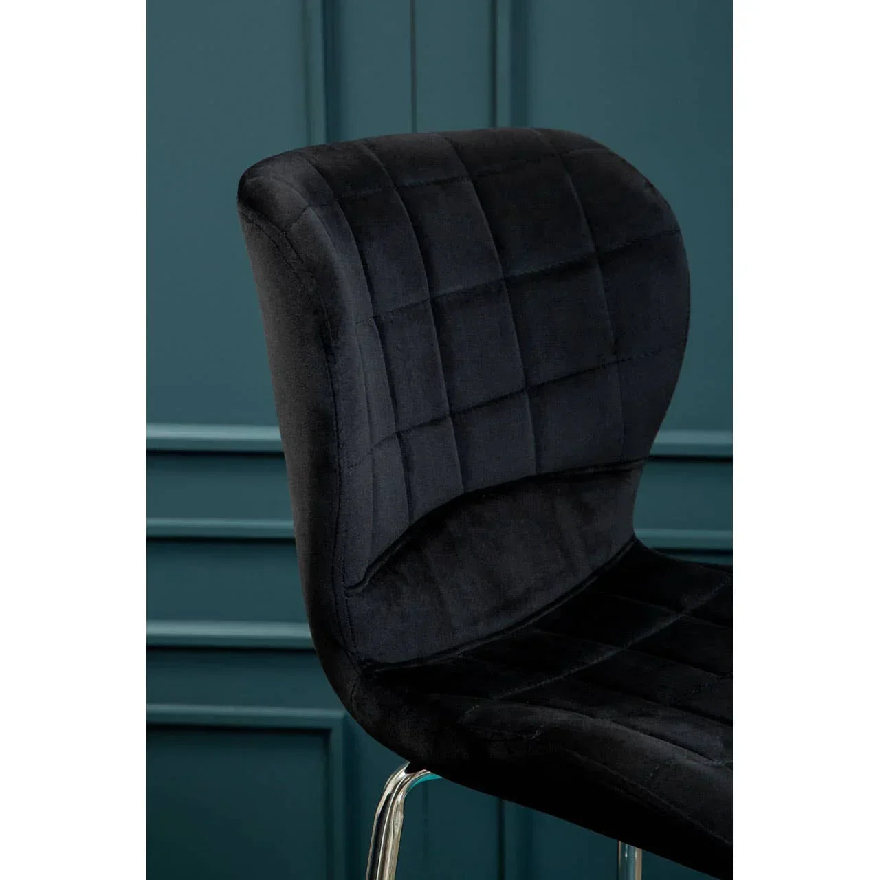 Black velvet dining chair with chrome legs and quilted backrest against teal wall