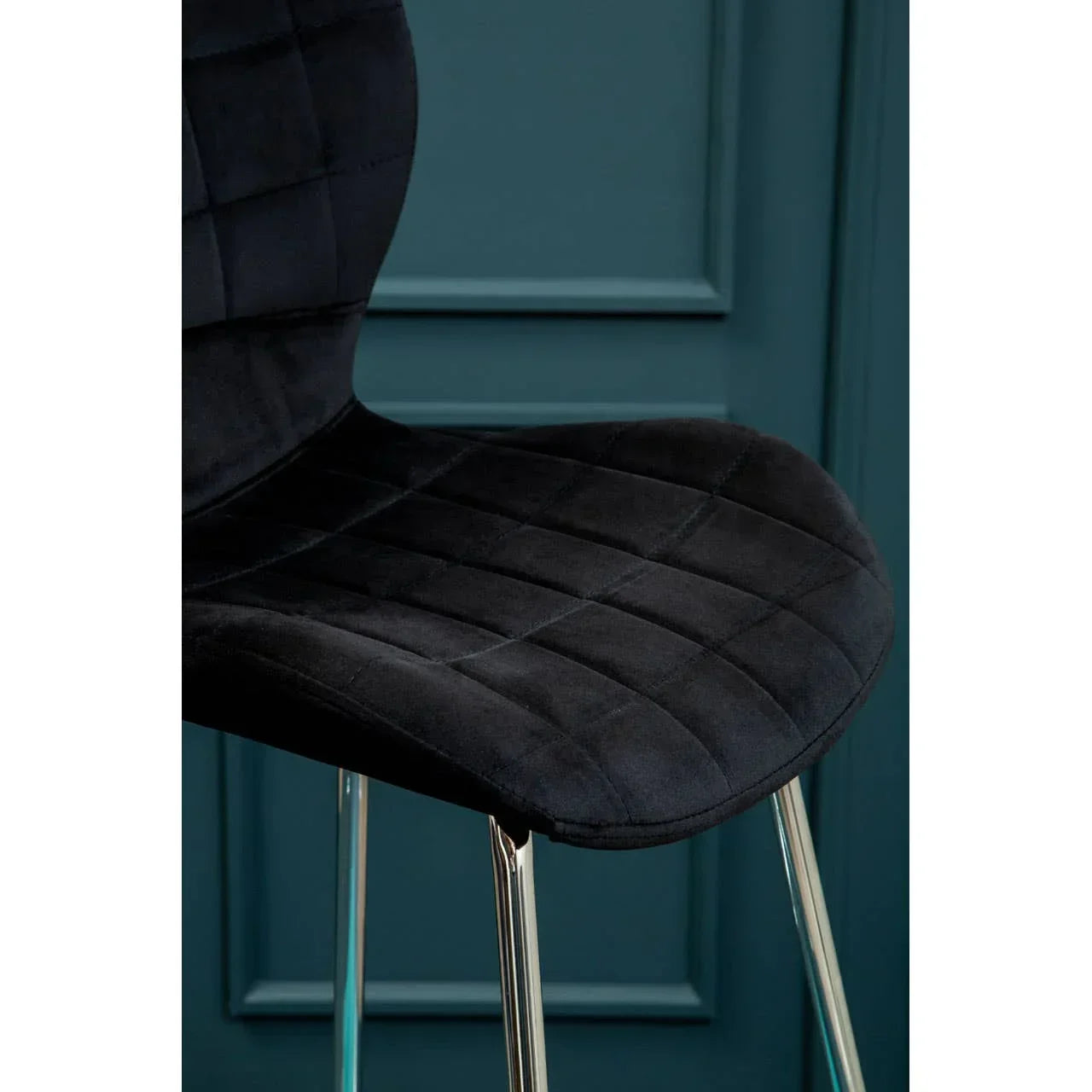Black velvet dining chair with chrome legs and quilted upholstery against teal wall