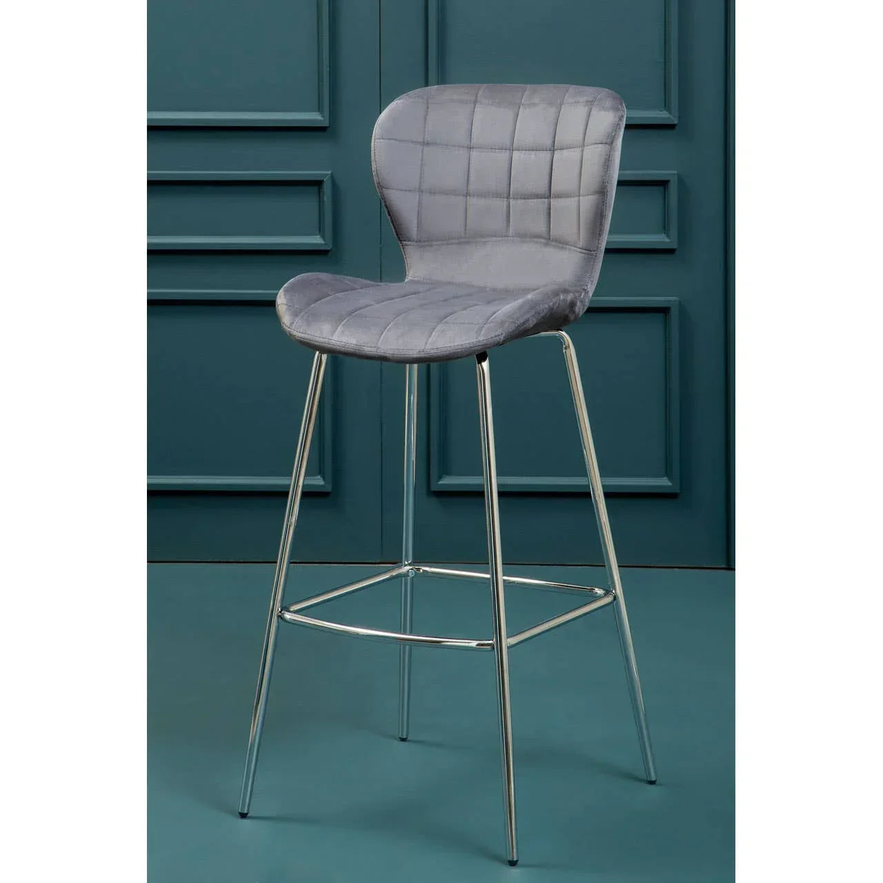 Grey velvet bar stool with chrome legs and quilted seat against teal wall