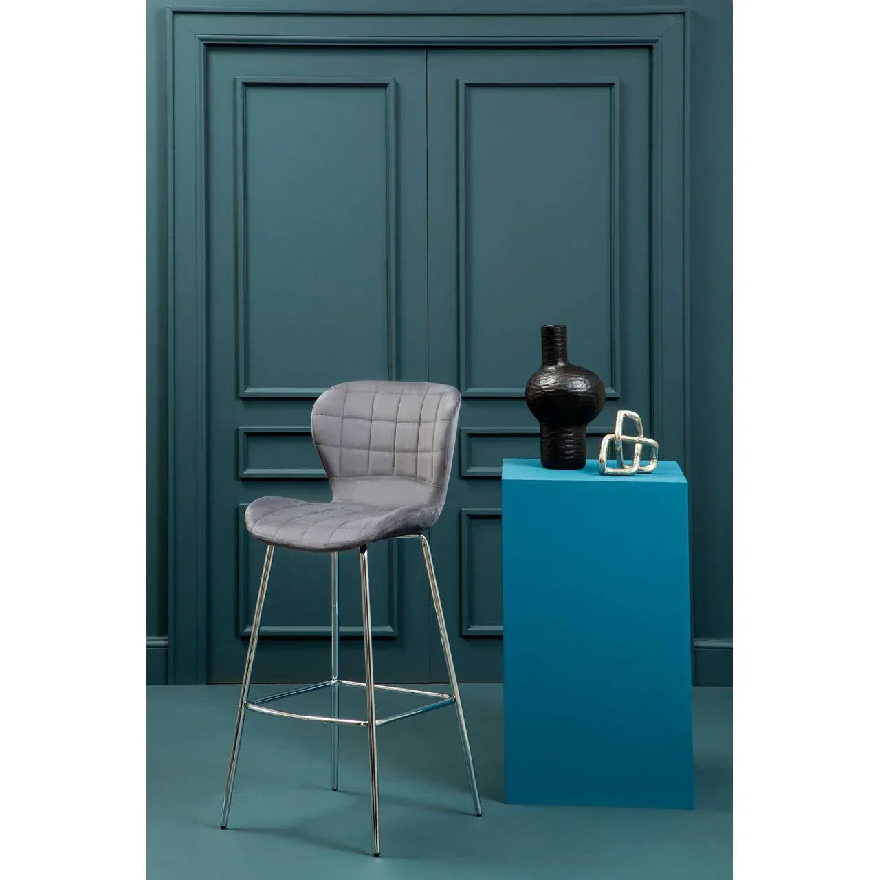Grey velvet bar stool with chrome legs beside blue display pedestal in modern interior