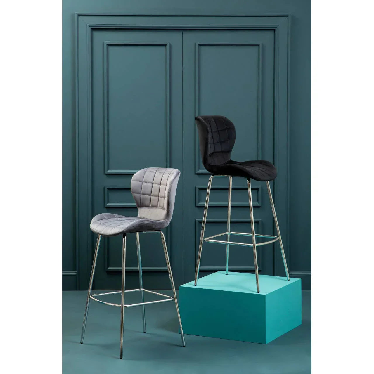 Grey and black velvet bar stools with chrome legs against teal wall panel backdrop