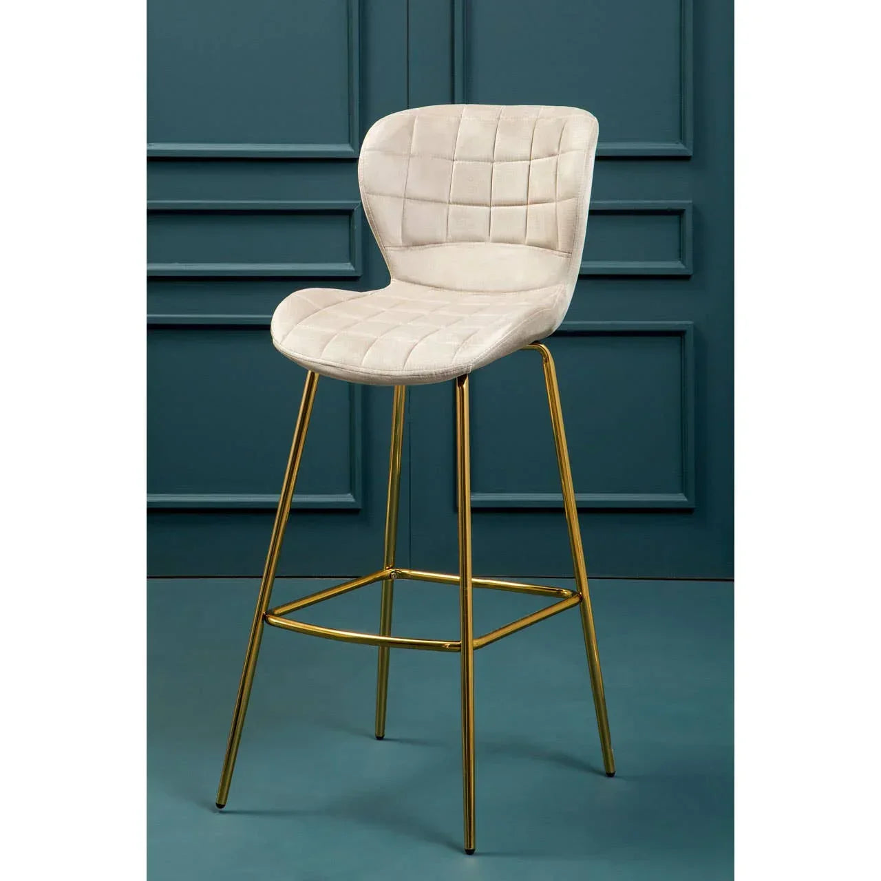Beige velvet bar stool with gold metal legs and grid-stitched seat against teal wall
