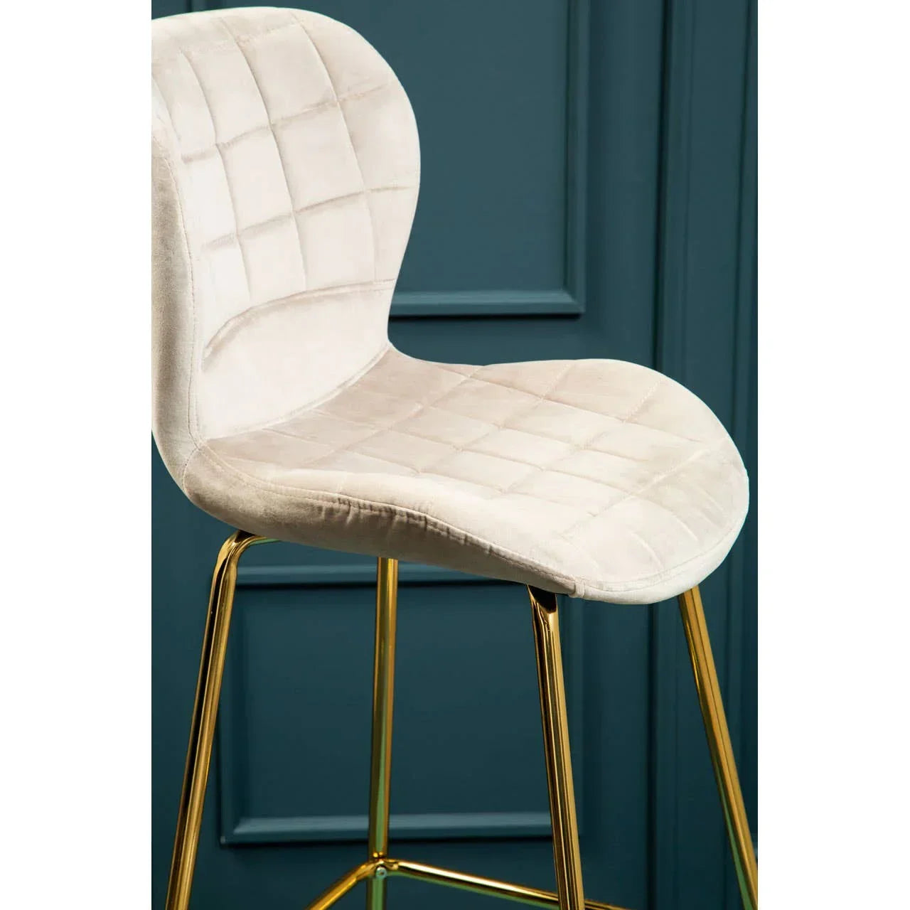 Cream velvet bar stool with quilted seat and gold legs against teal panel wall