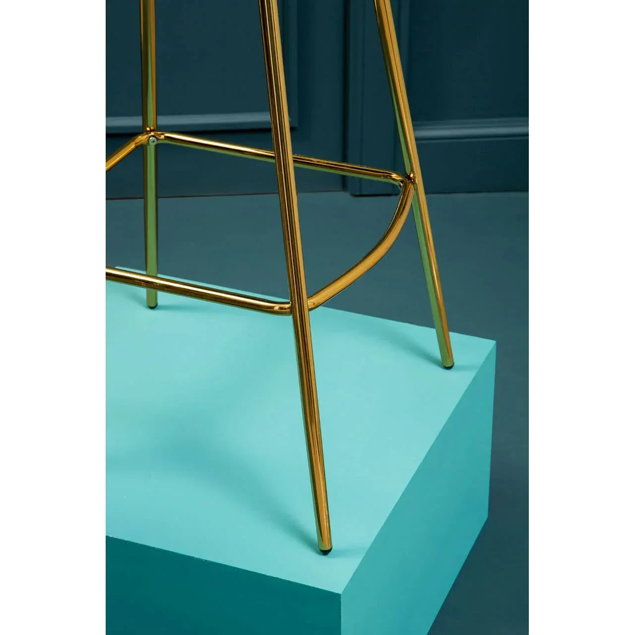 Gold metal bar stool legs on a turquoise platform with dark blue background