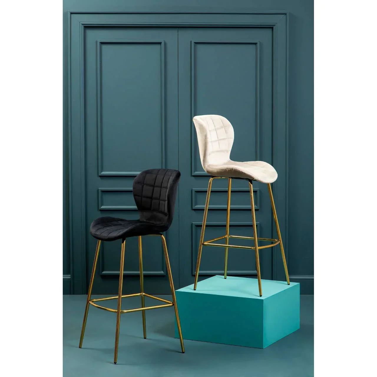 Black and cream velvet bar stools with gold legs, quilted seats, set against teal panel wall