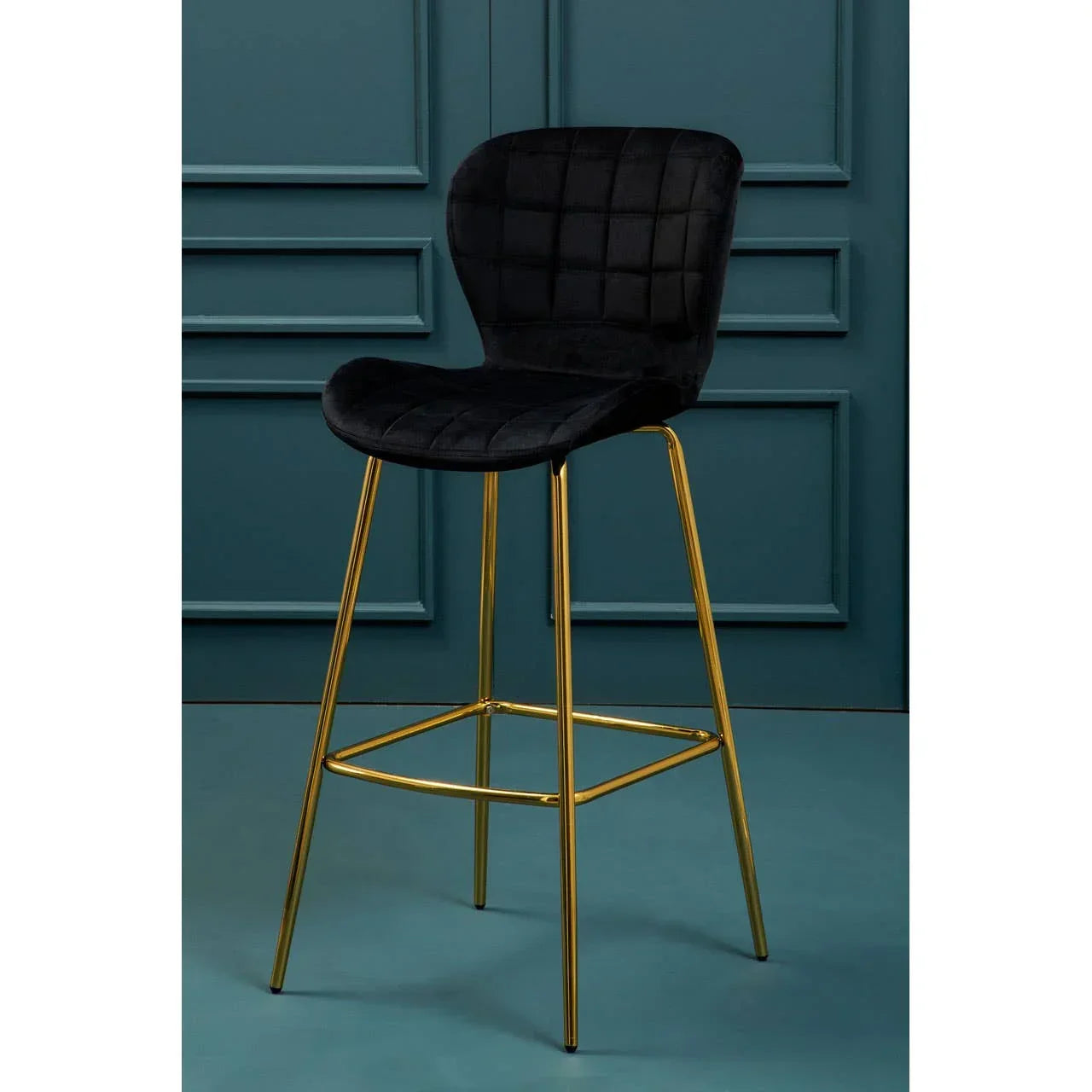 Black velvet bar stool with gold metal legs and square stitched backrest against teal wall