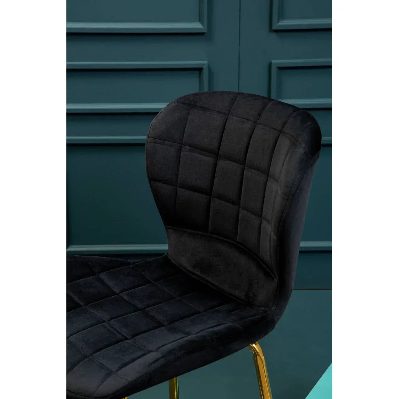 Black velvet dining chair with gold legs and quilted seat against teal wall