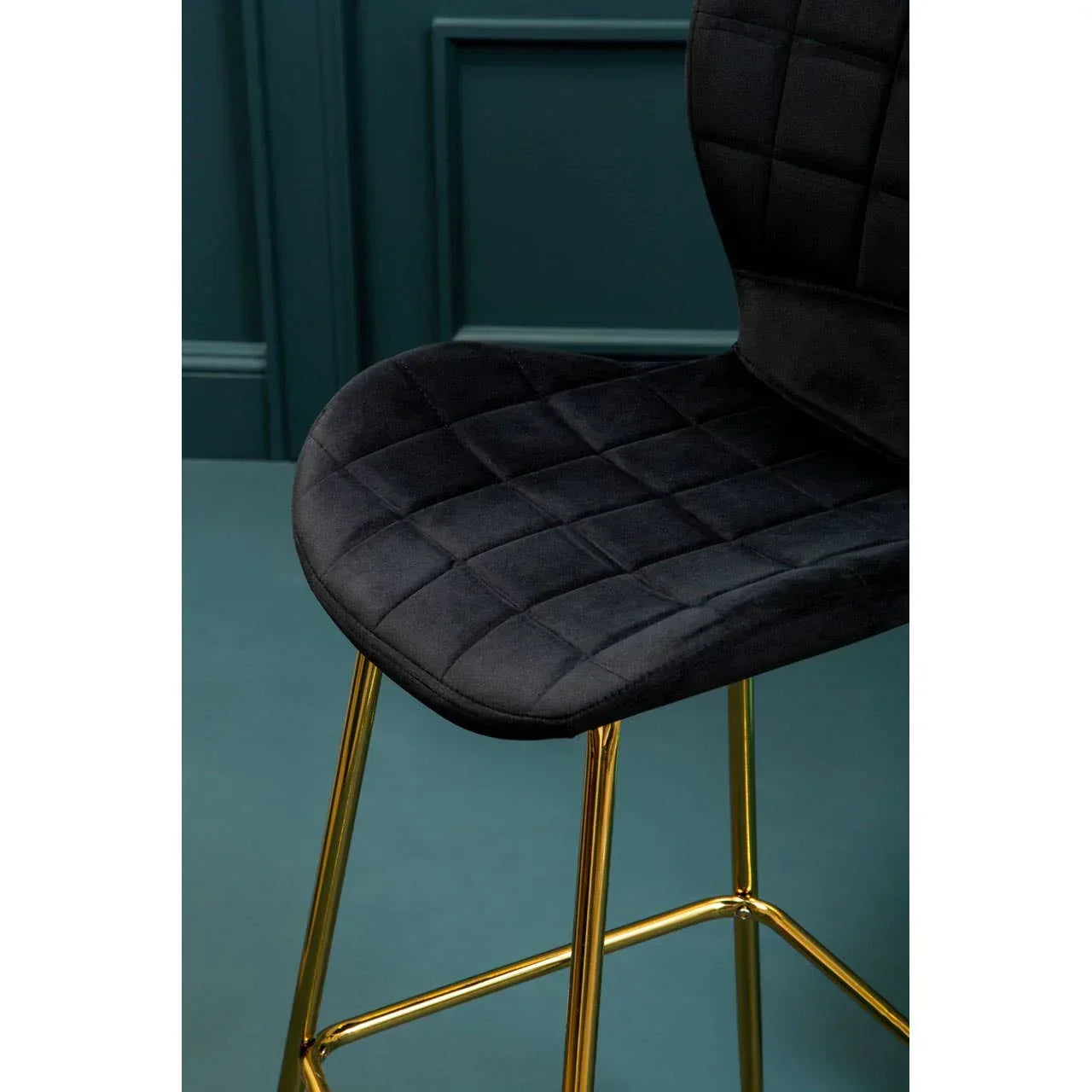Black velvet bar stool with gold metal legs against teal paneled wall