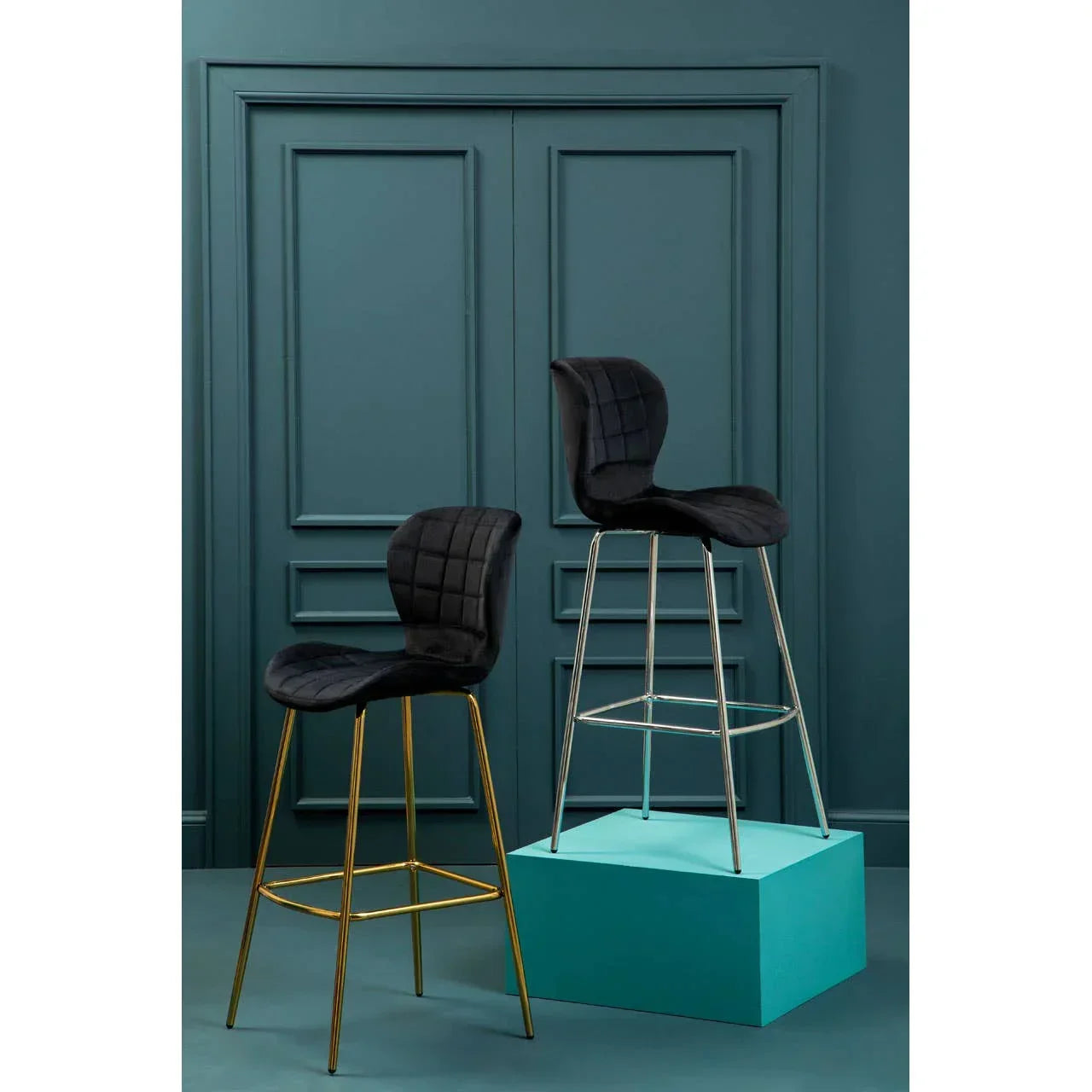Black velvet bar stools with gold and chrome legs against teal wall panel backdrop