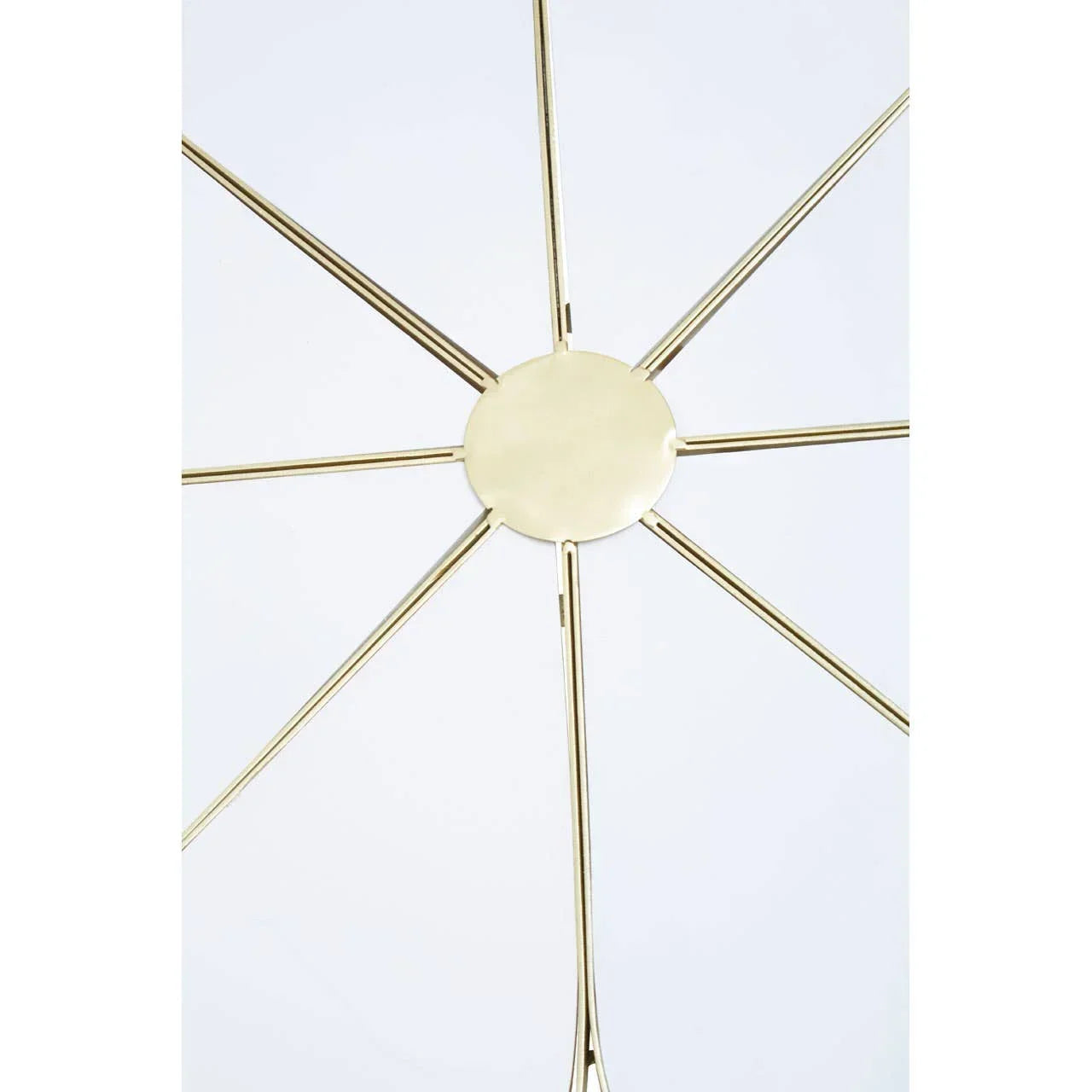 Gold metal wall art with radiating spokes and circular center on white background