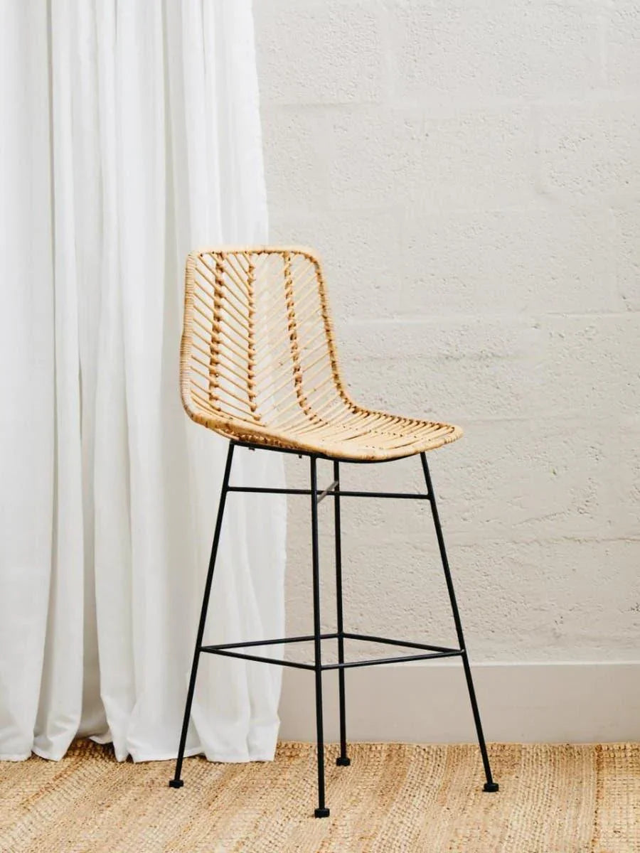Rattan bar stool with black metal legs on woven rug in minimalist room