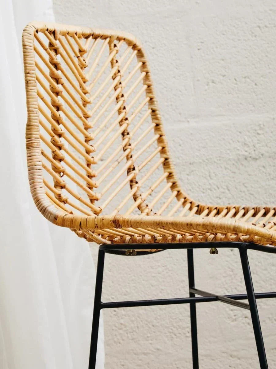 Natural rattan bar stool with black metal legs against a light textured wall