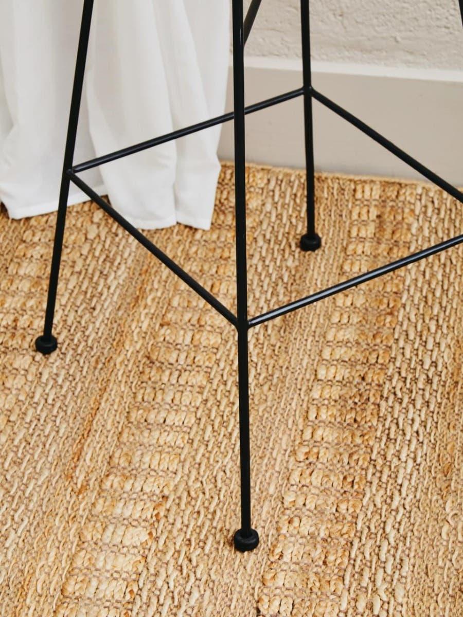 Black metal bar stool legs on woven rug next to white curtain