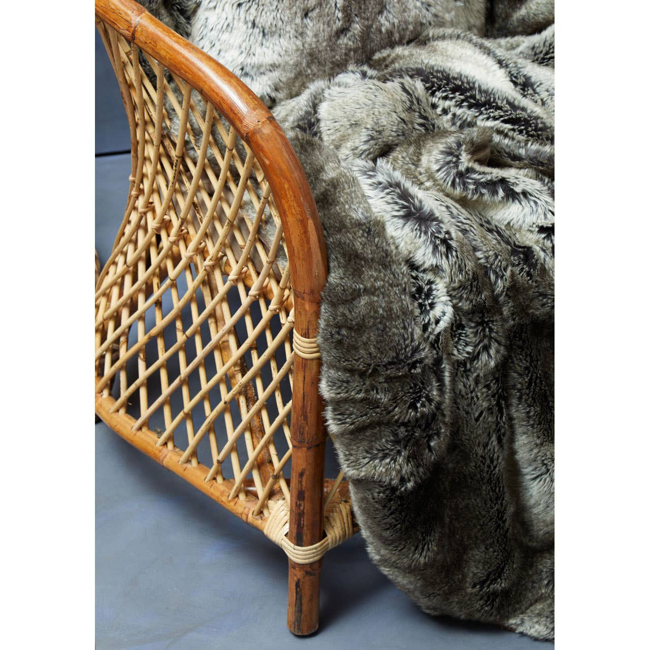 Natural rattan chair with a high backrest, featuring a woven design and a light wood finish, partially covered by a soft, textured gray throw blanket, set against a blue background