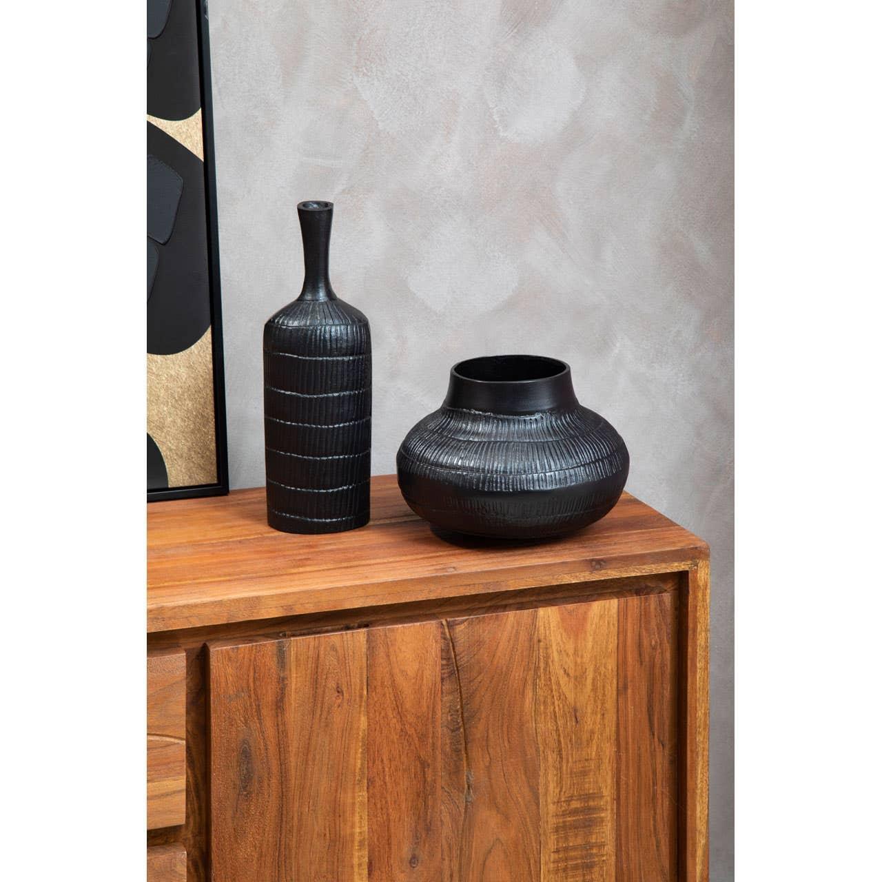 Black ceramic vase set on wooden sideboard against textured wall