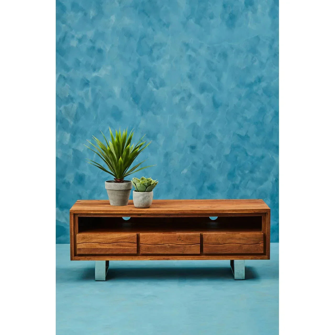 Solid wood TV unit with three drawers, open shelf, and metal legs against blue wall
