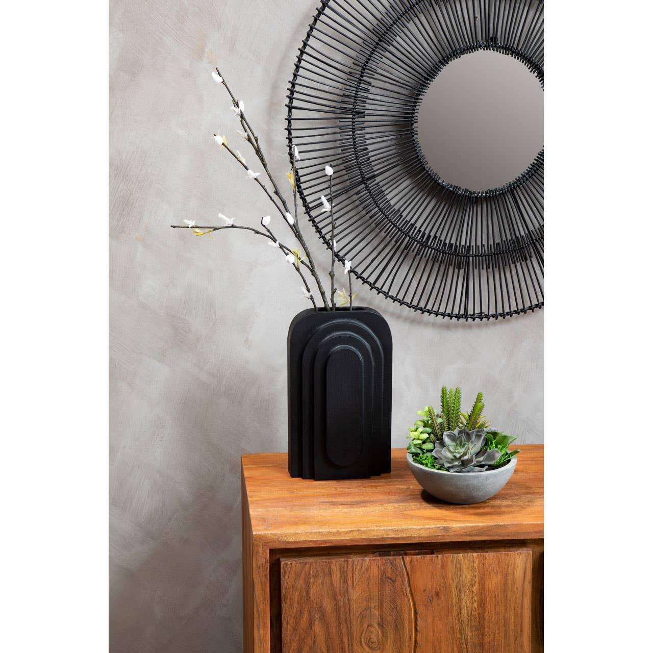 Wooden sideboard with black vase, faux branches, concrete planter, and round wall mirror