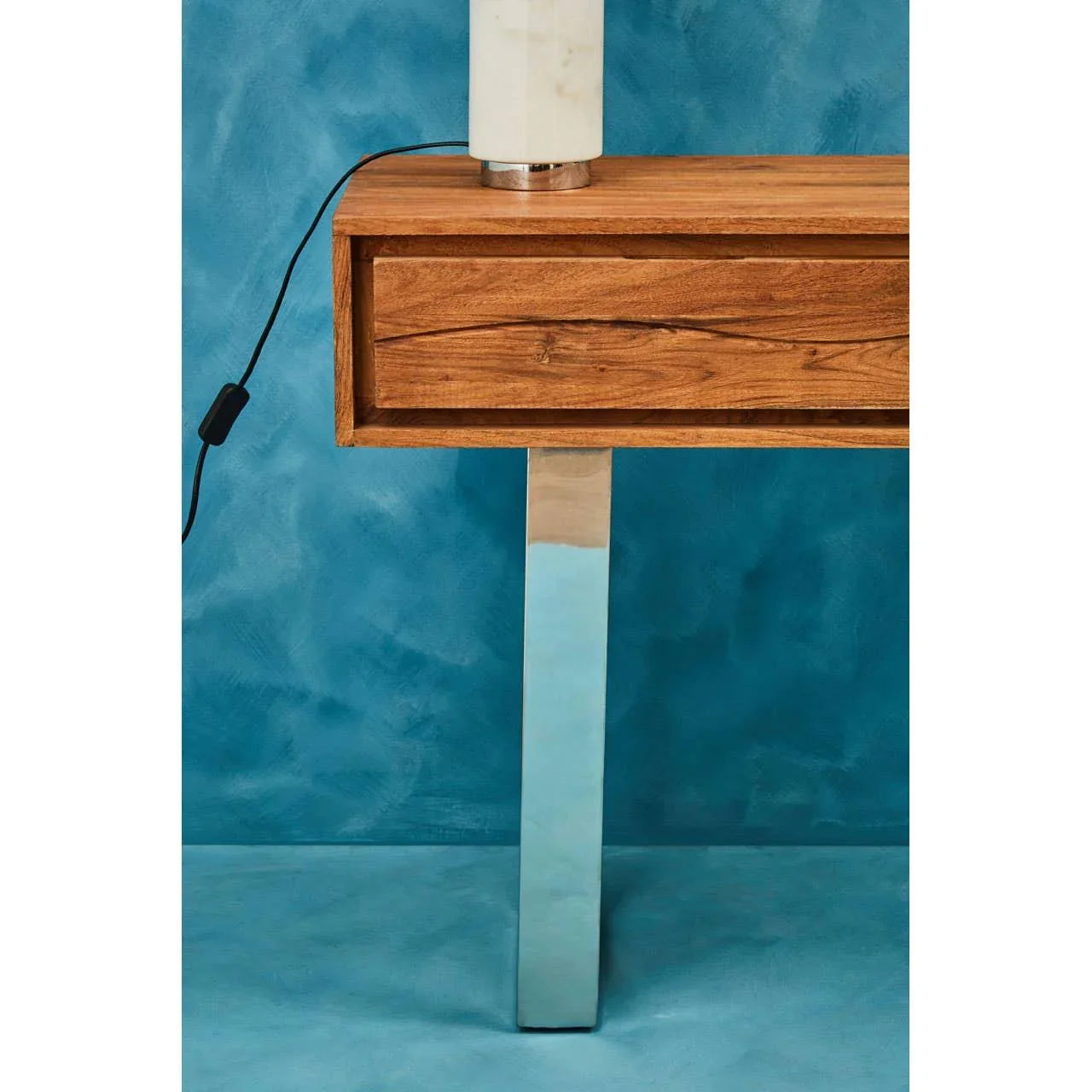 Wood console table with stainless steel leg against blue wall, single drawer visible