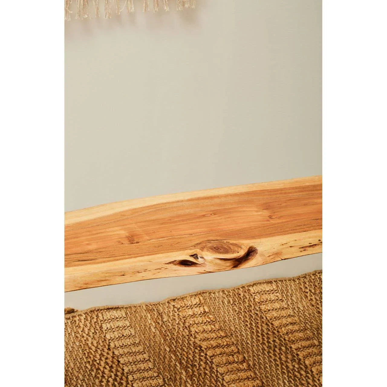 Close up of wooden dining table edge with natural grain, shown above woven rug