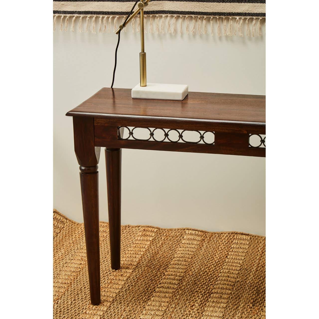 Dark wood console table with carved detail and brass lamp on woven jute rug