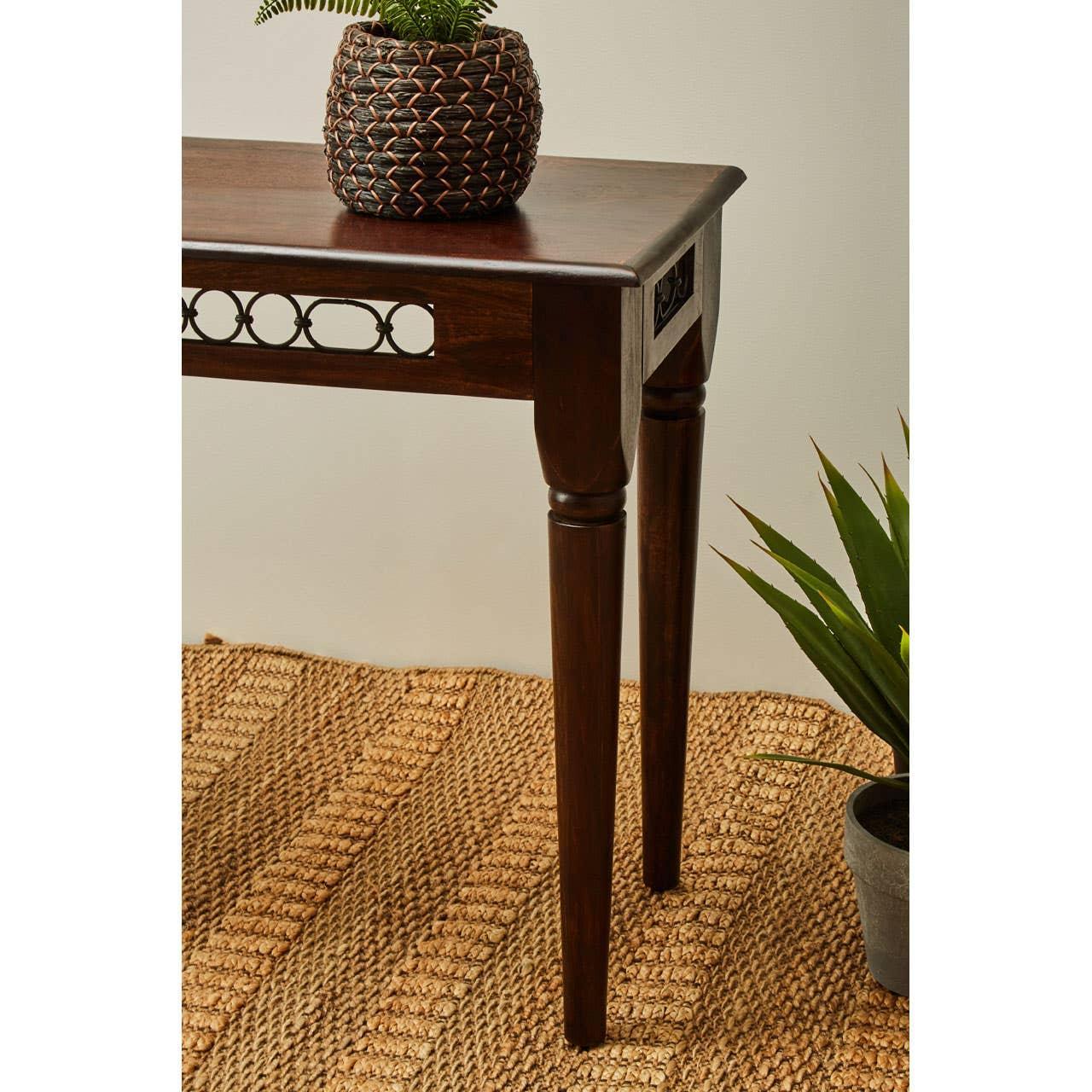 Dark wood console table with carved detail and decorative plant on woven rug