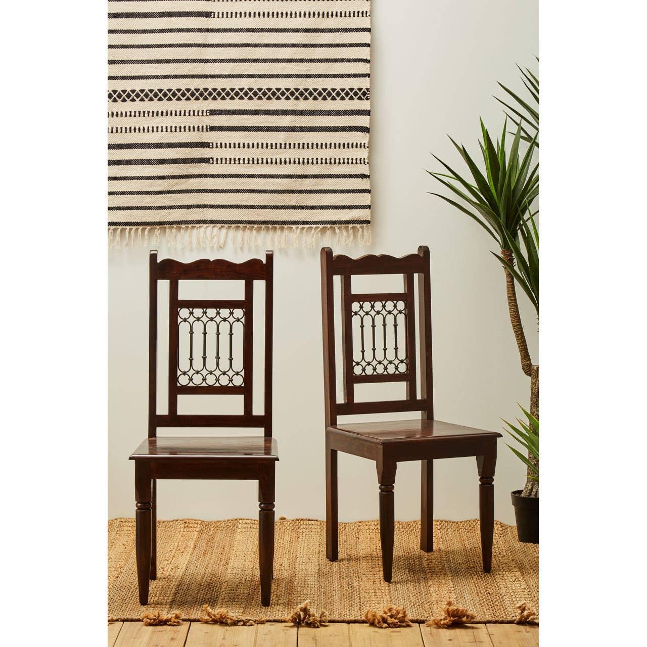 Pair of dark wood dining chairs with carved backrest on woven rug next to indoor plant