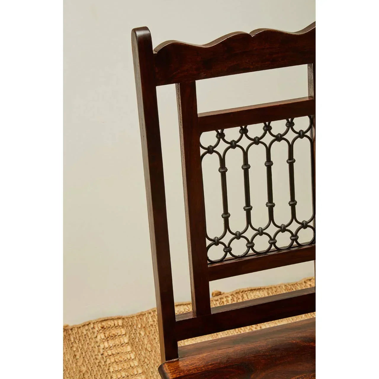 Dark wood dining chair with decorative metal backrest detail on woven rug