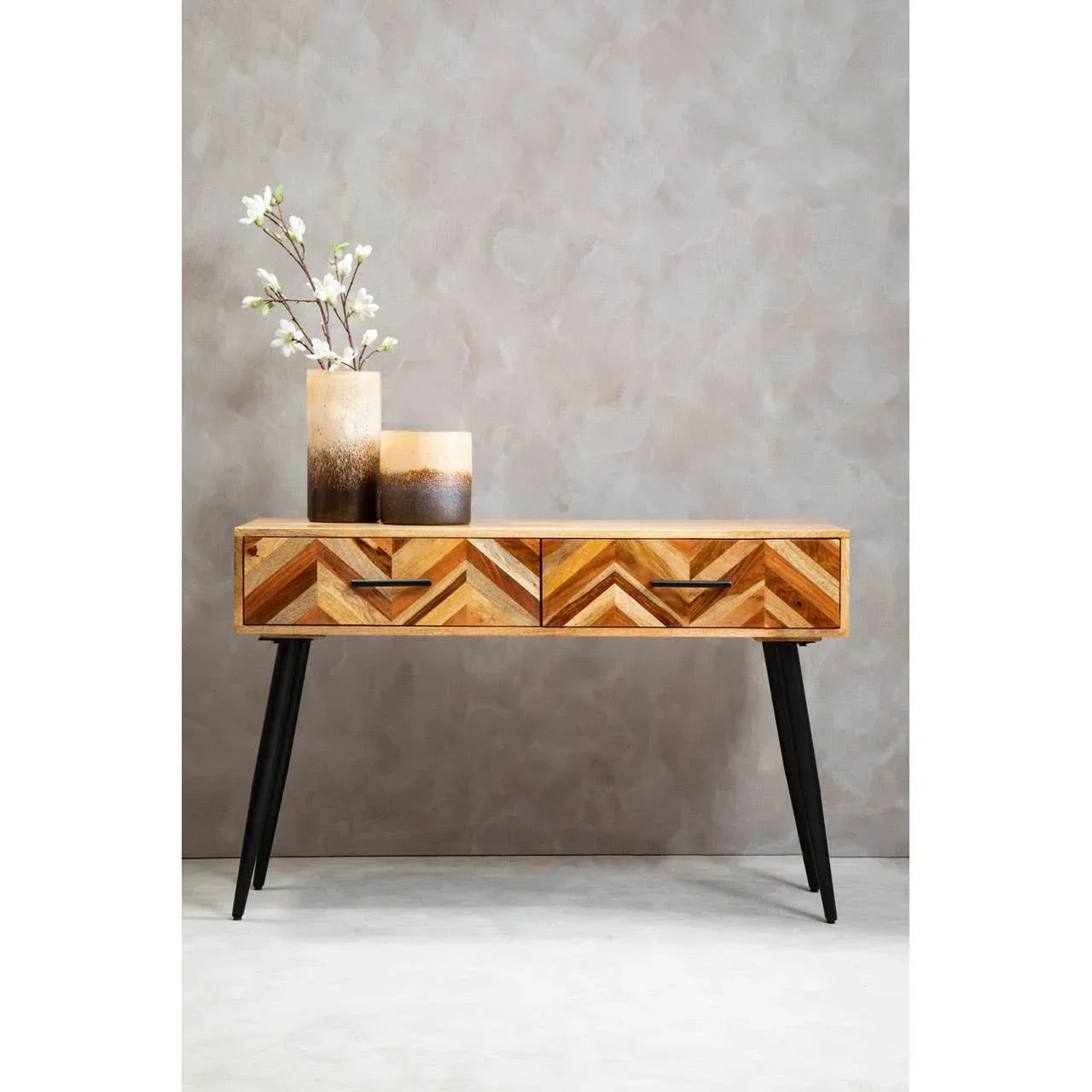Chevron wood console table with black legs, two drawers, and decorative vases on top