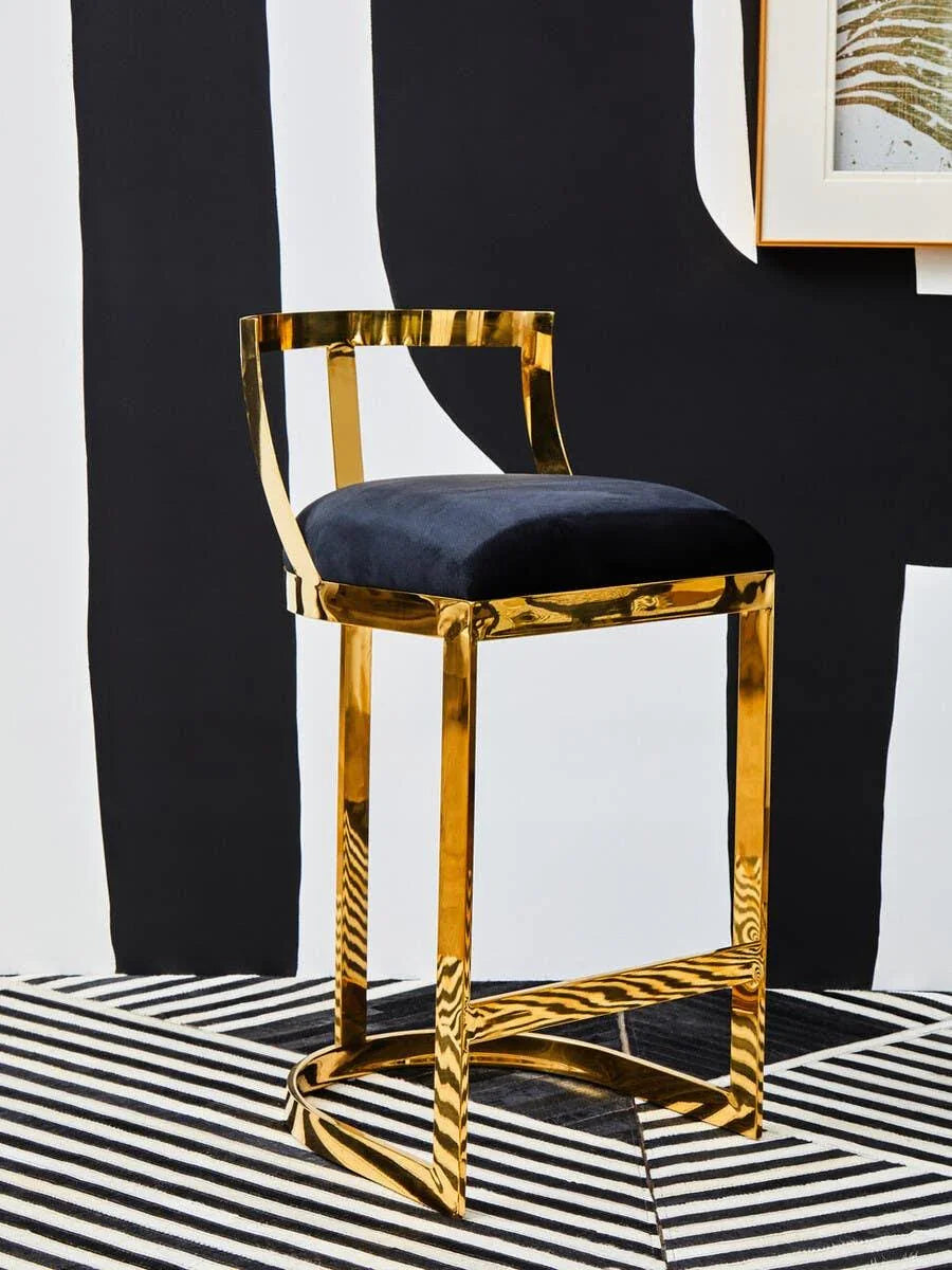 Gold metal bar stool with black velvet seat on striped rug and abstract wall background