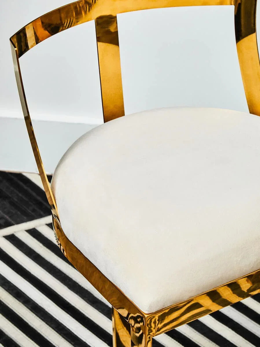 Gold metal dining chair with white upholstered seat on black and white striped rug