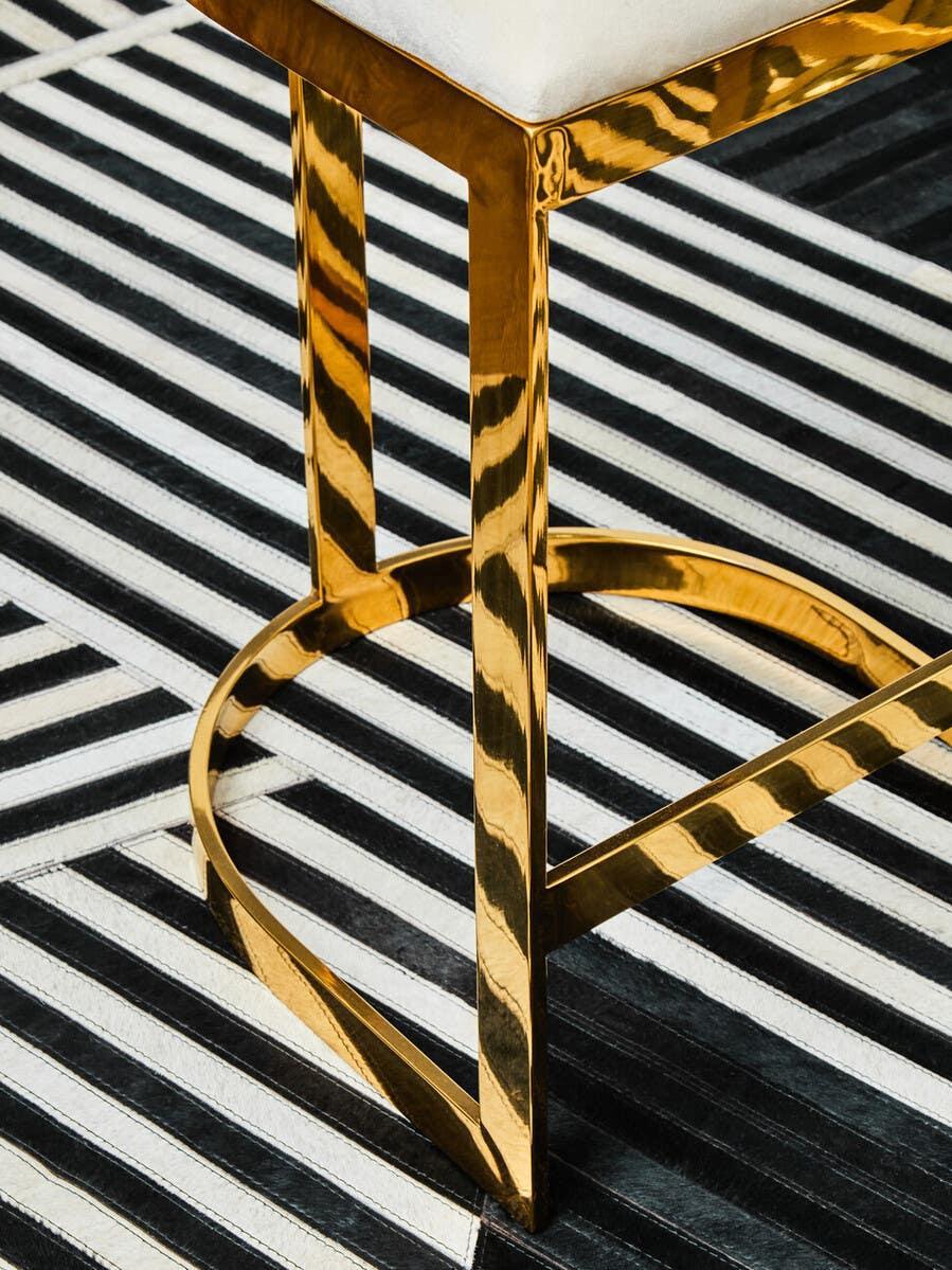 Gold metal dining chair leg with cream seat on black and white striped rug