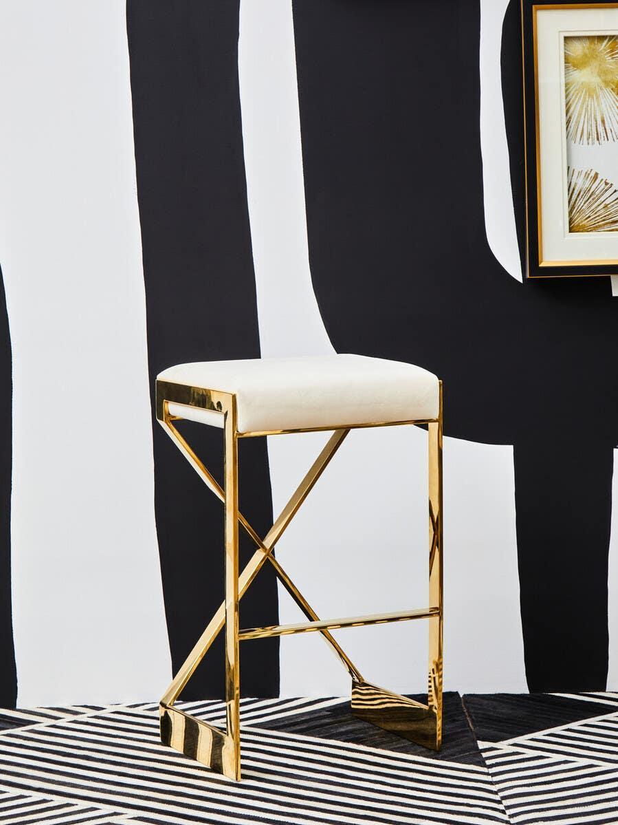 Gold metal bar stool with white cushioned seat on black and white patterned rug