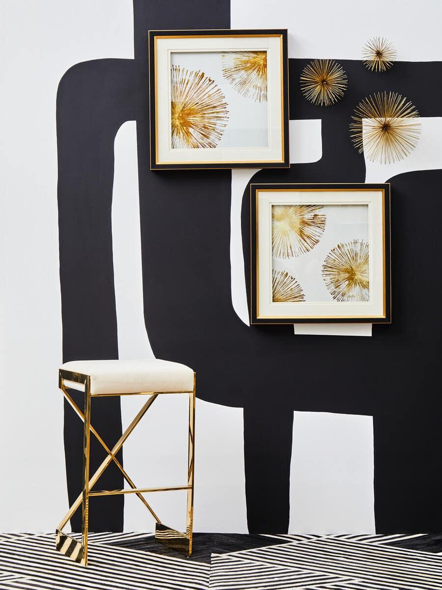 Gold metal bar stool with cream seat beside modern wall art and geometric wall decor